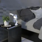 Beli projektor zeka astronaut stoji na crnom noćnom stočiću pored biljke, knjiga i kreveta